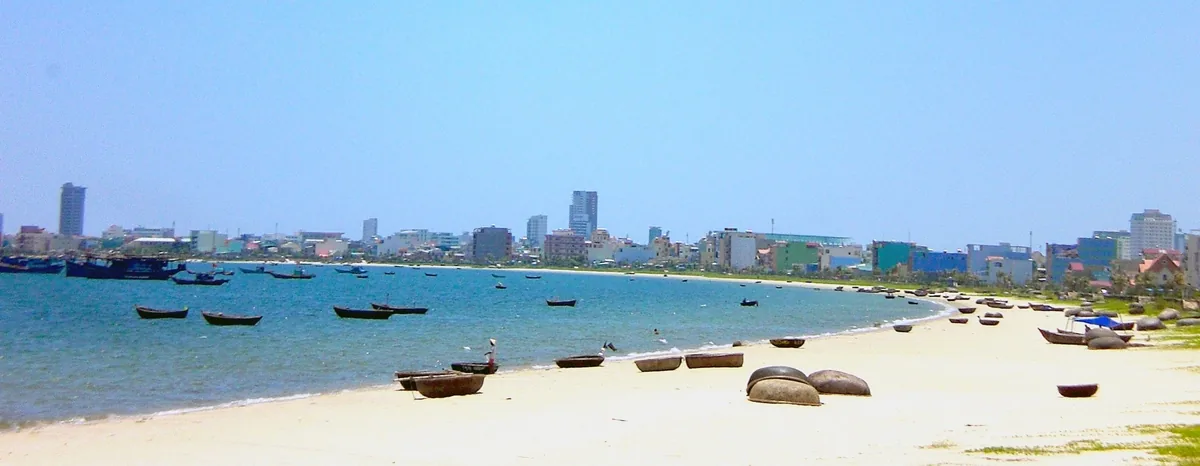 Thuyền thúng nằm trên bãi cát, xa xa là dãy nhà cao tầng Đà Nẵng